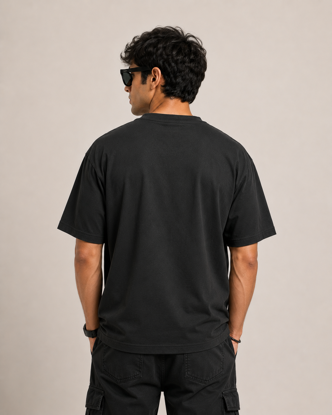 Person wearing a black t-shirt and sunglasses, standing against a beige background